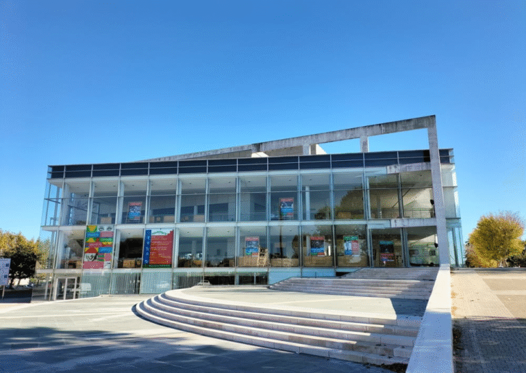 El Teatre Nacional de Narbona 1 Edifici modern del Teatre + Cinéma Scene Nationale Grand Narbonne amb façana de vidre amb cartells d'esdeveniments visibles des de l'exterior